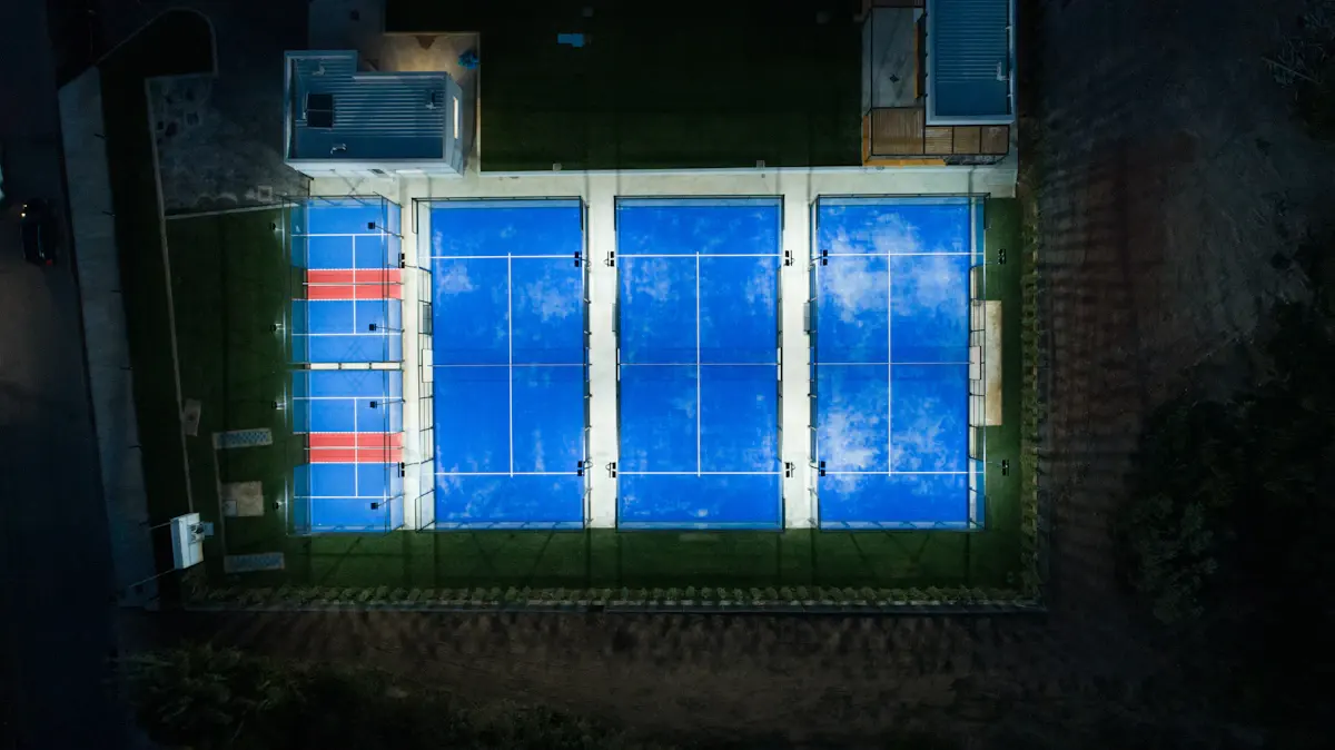 Aerial view of floodlit blue padel courts at night beside a clubhouse